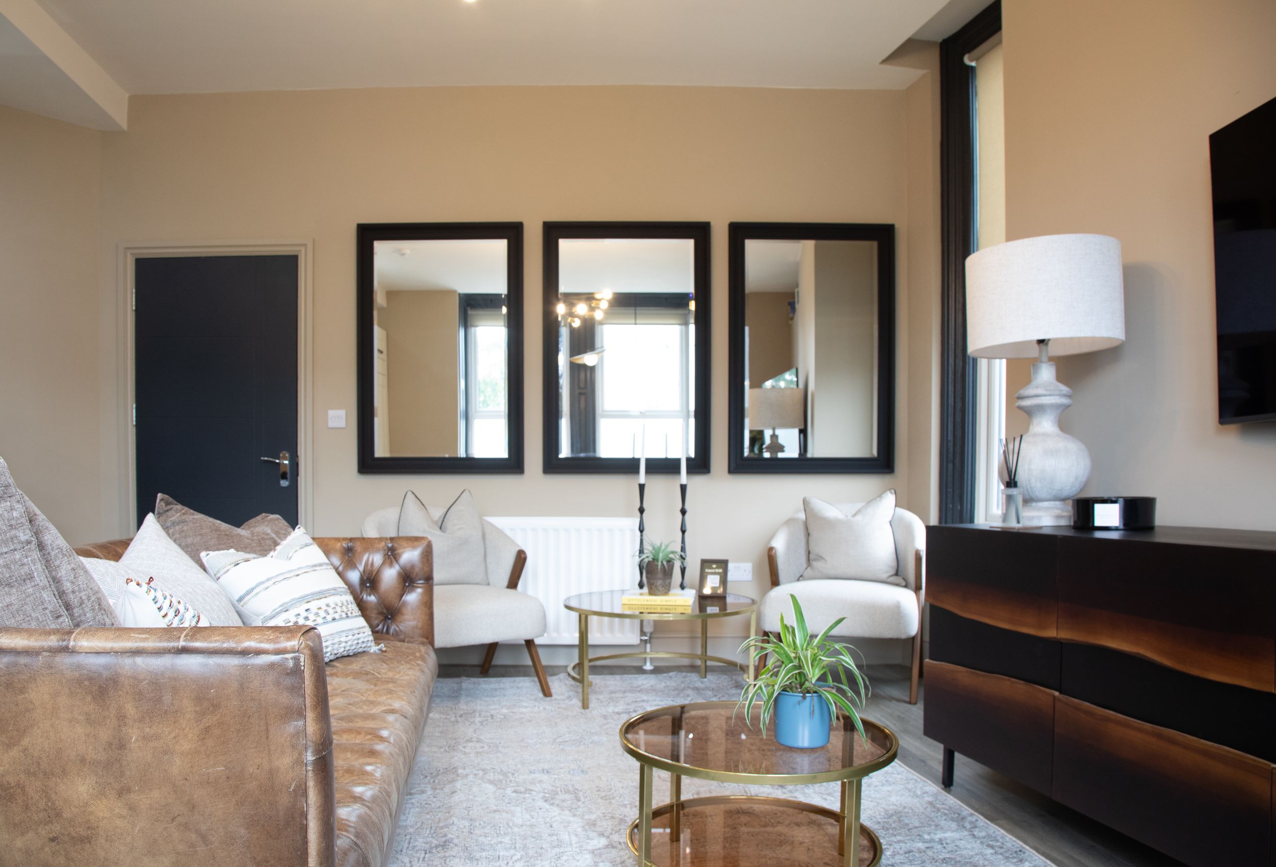 Elegant living room with leather sofa, white armchairs, gold coffee table and triple mirrors.