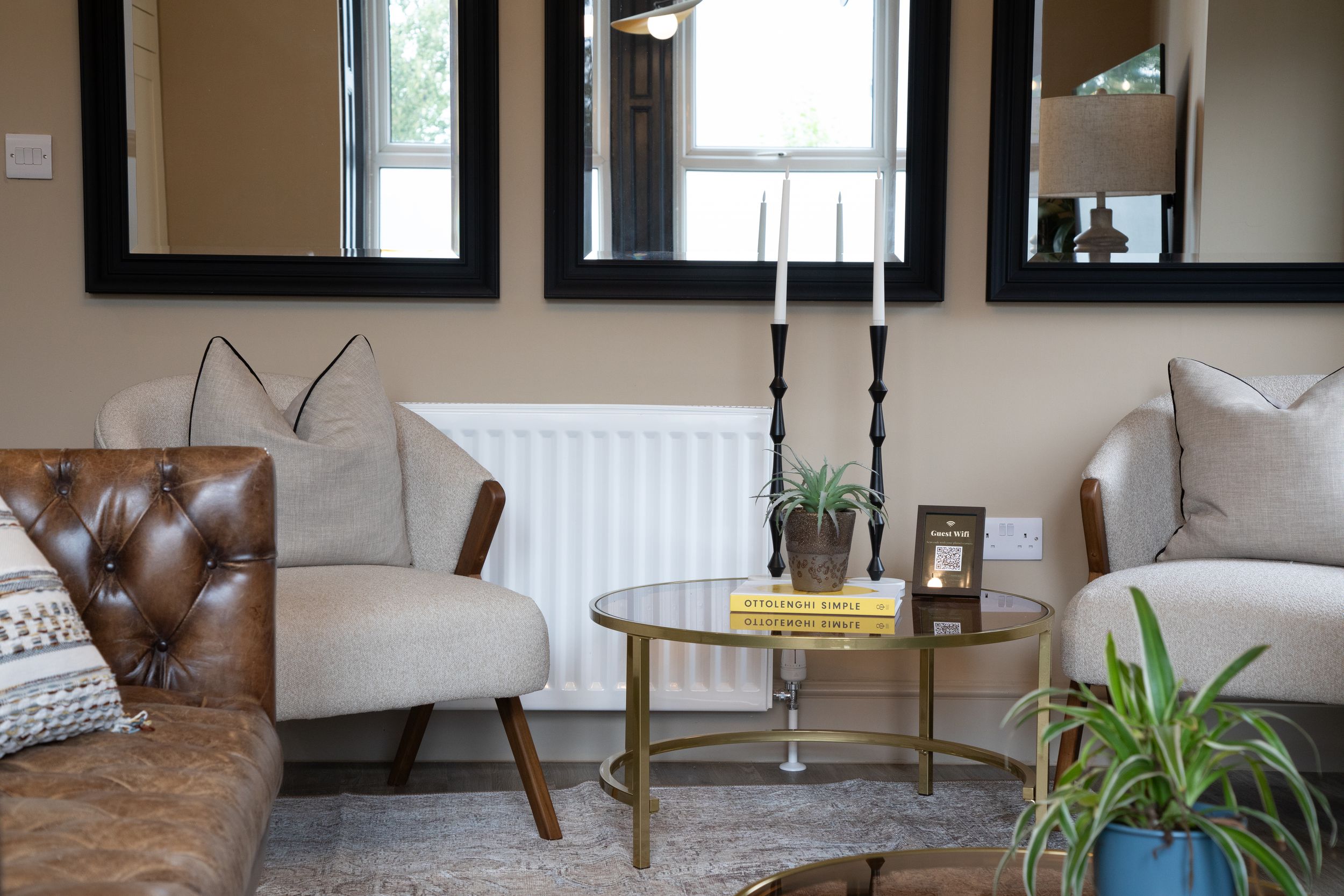 Stylish living room corner with tufted leather sofa, glass coffee table and decorative mirrors.