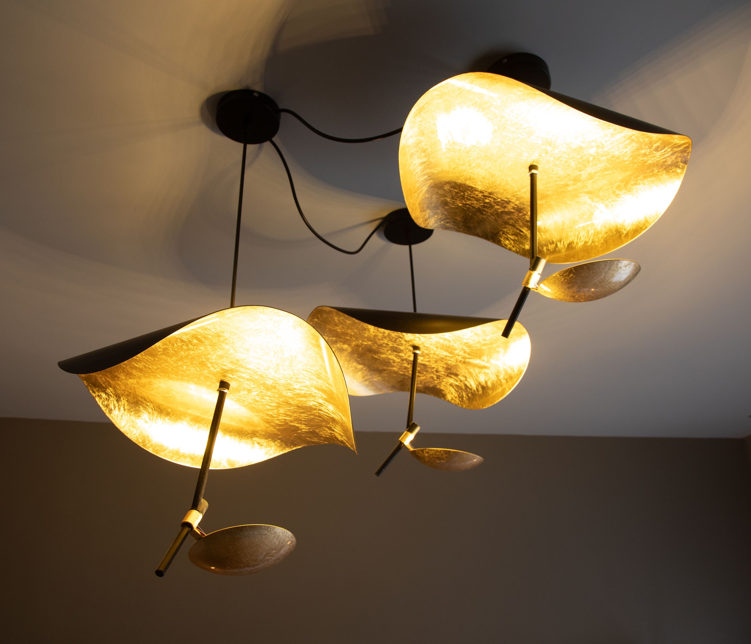 Modern gold leaf pendant lights cluster on ceiling, creating warm ambient glow with sculptural curved shades.
