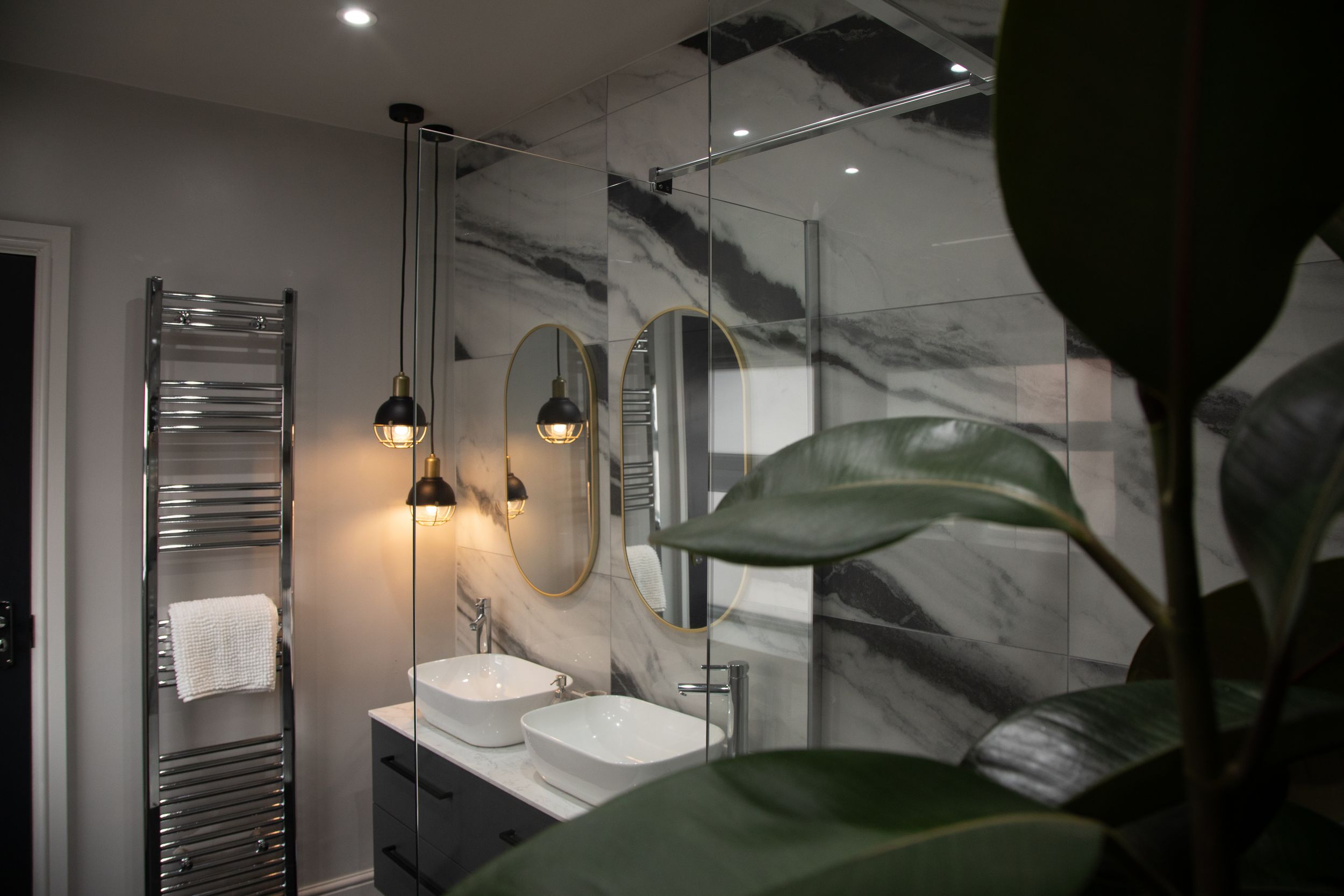 Modern bathroom with marble walls, dual vessel sinks, round mirrors, pendant lights, and a heated towel rail.