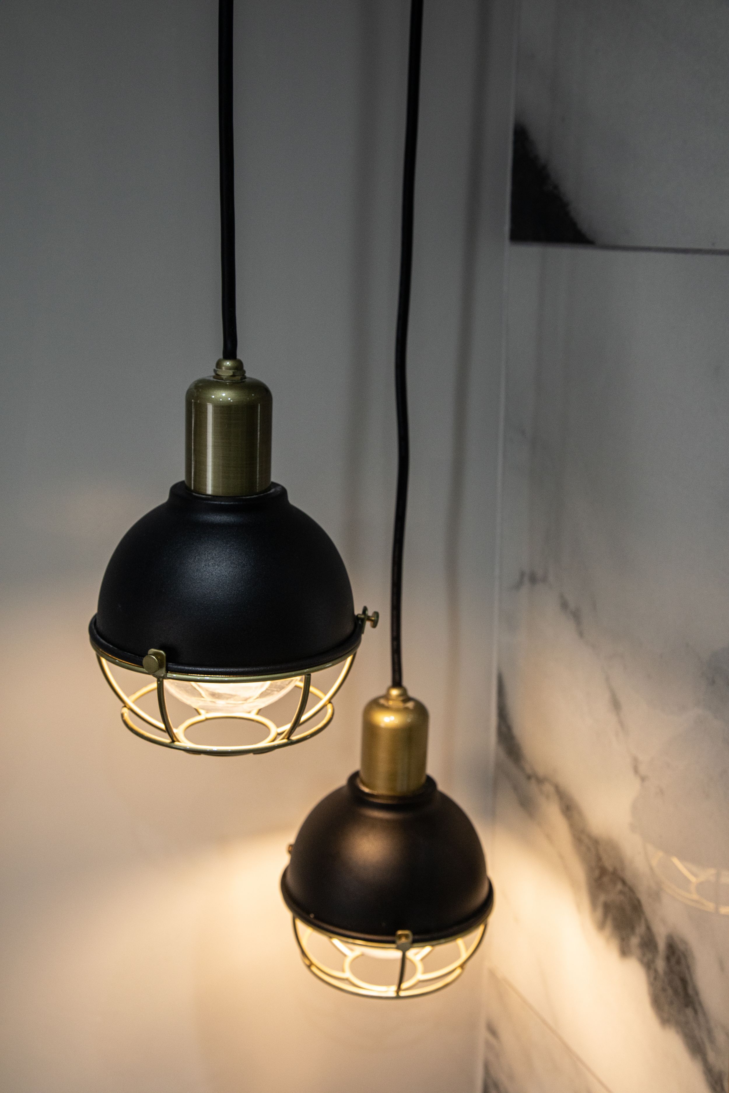 Two black industrial pendant lights with brass fittings hang from black cords against a marble wall.