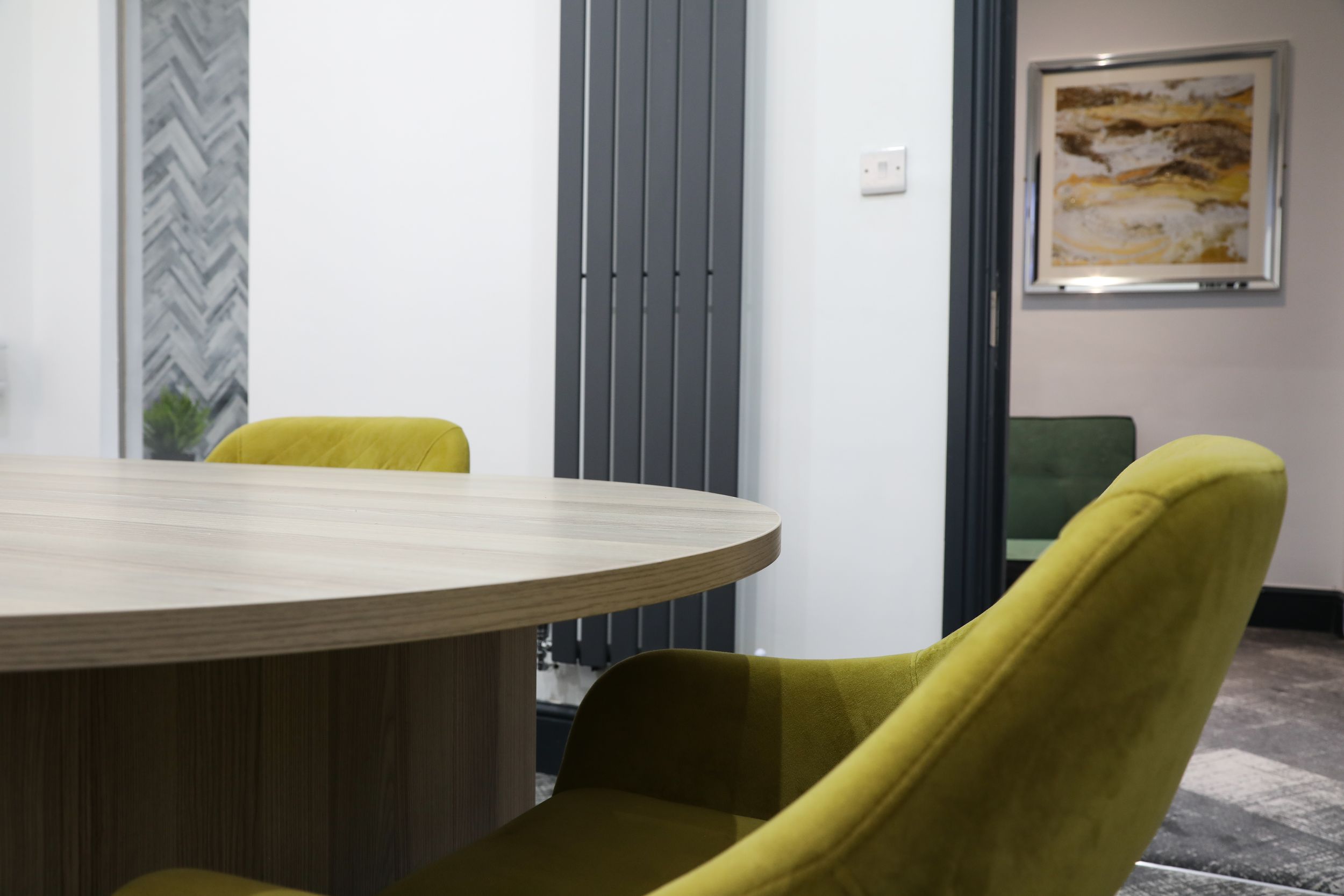 Modern meeting room with round wooden table and olive green velvet chairs with radiator.