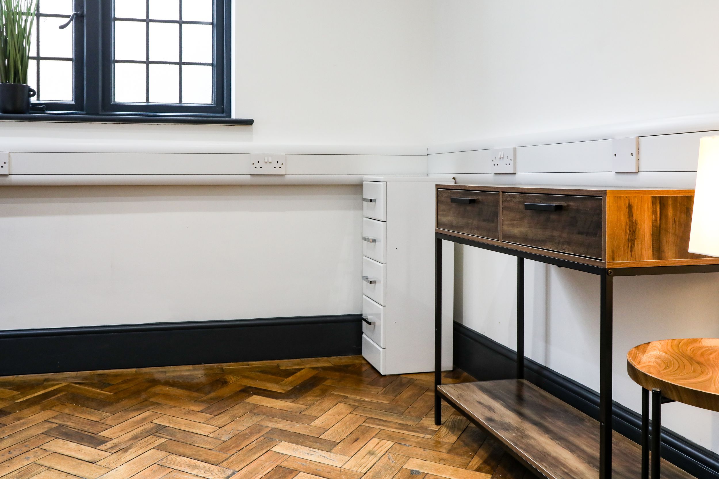 Bright office space featuring herringbone parquet flooring, built-in white drawers and wooden desk.