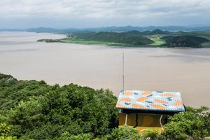 Aerial view of a yellow building with colorful roof amid lush greenery overlooking a wide river and islands.