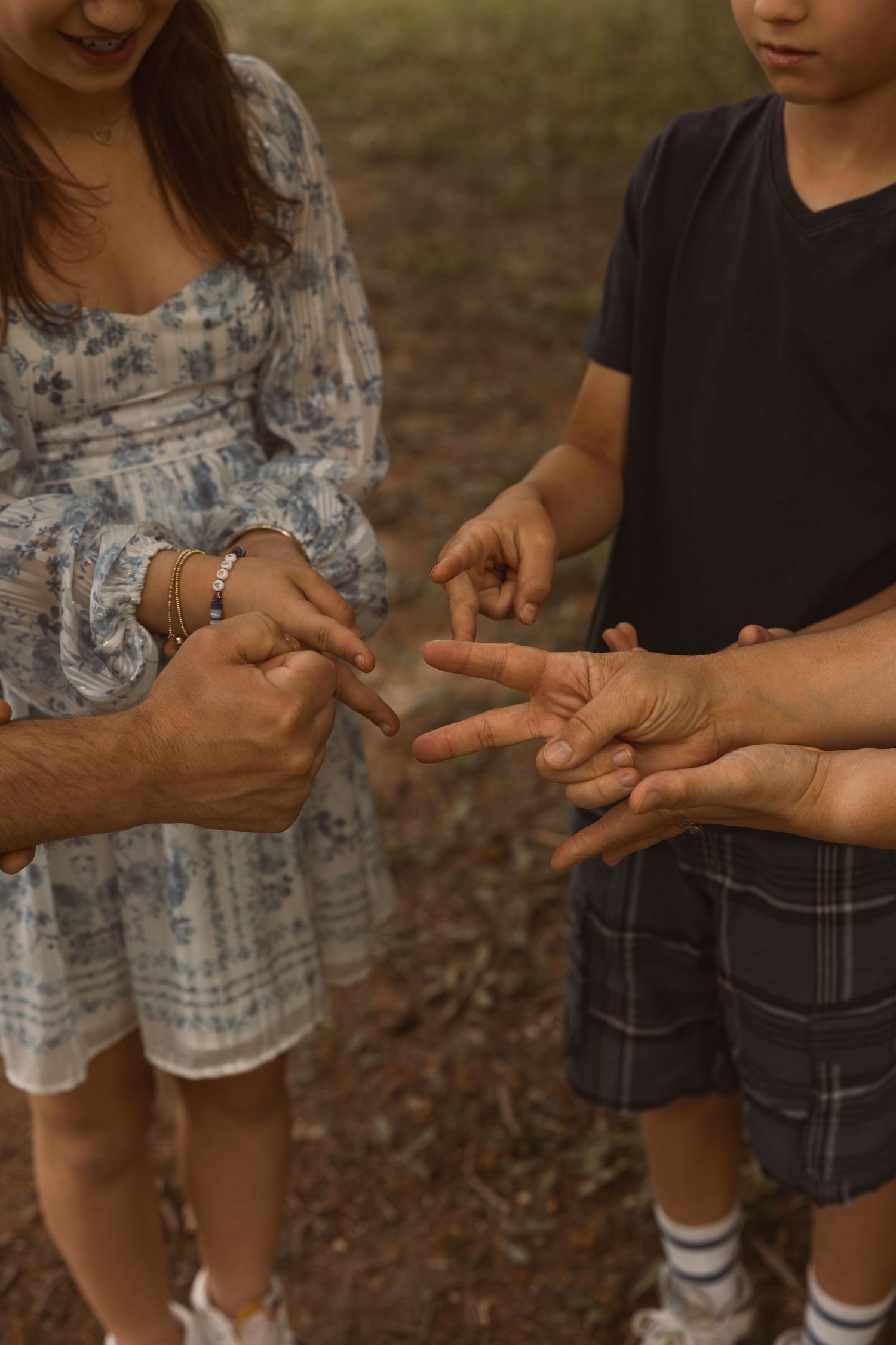 Family playing rock paper scissors outdoors, children and adults hands visible in a forest setting.