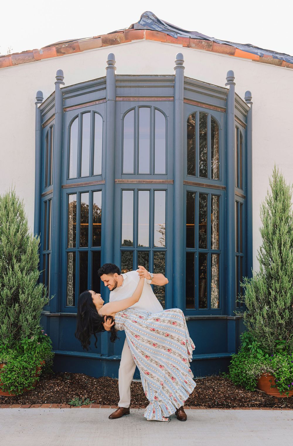 Couple sharing a romantic dip pose in front of a blue arched window at an elegant venue.