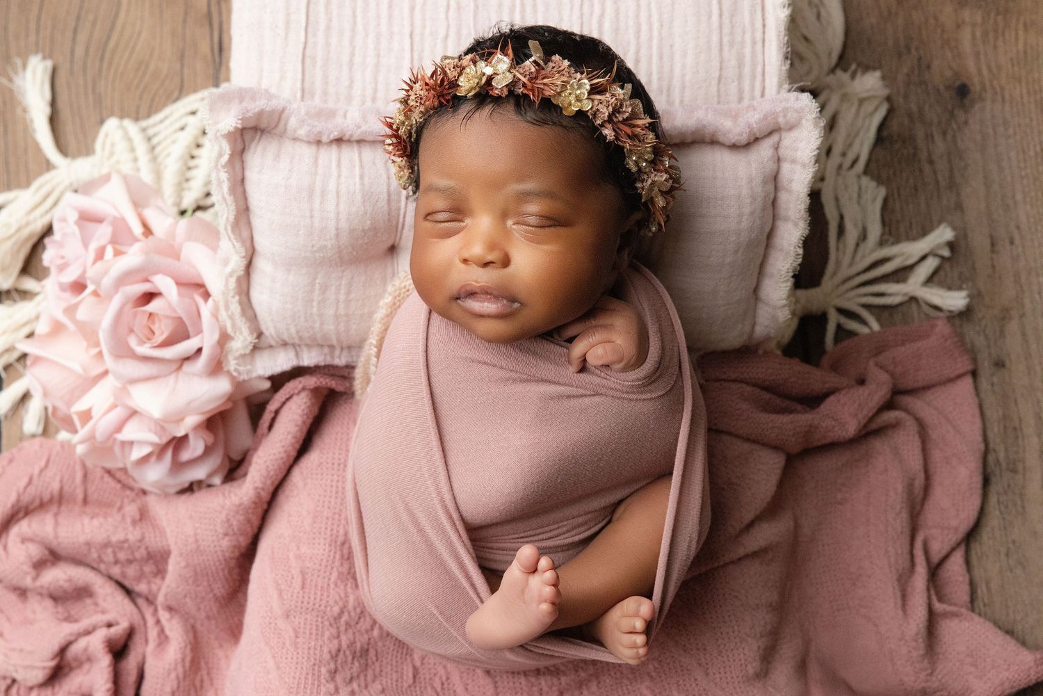 Newborn baby wrapped in teal swaddle holding green knit bear toy, resting in decorative bucket.