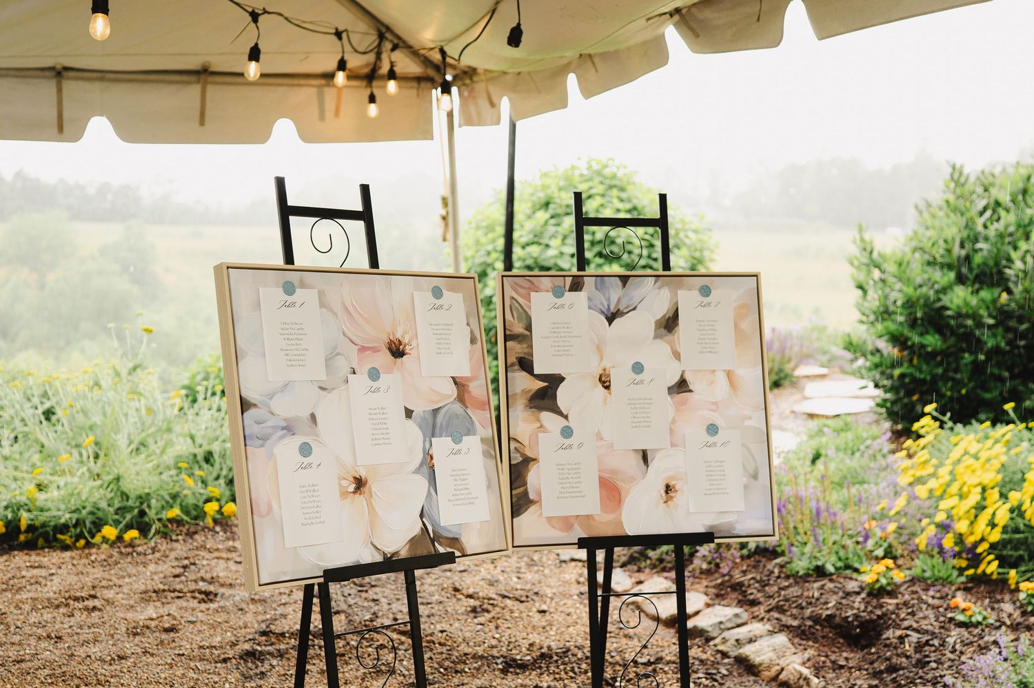 Small glass vases with colorful pink and yellow flowers on a white table with blue floral runner at an outdoor wedding reception.