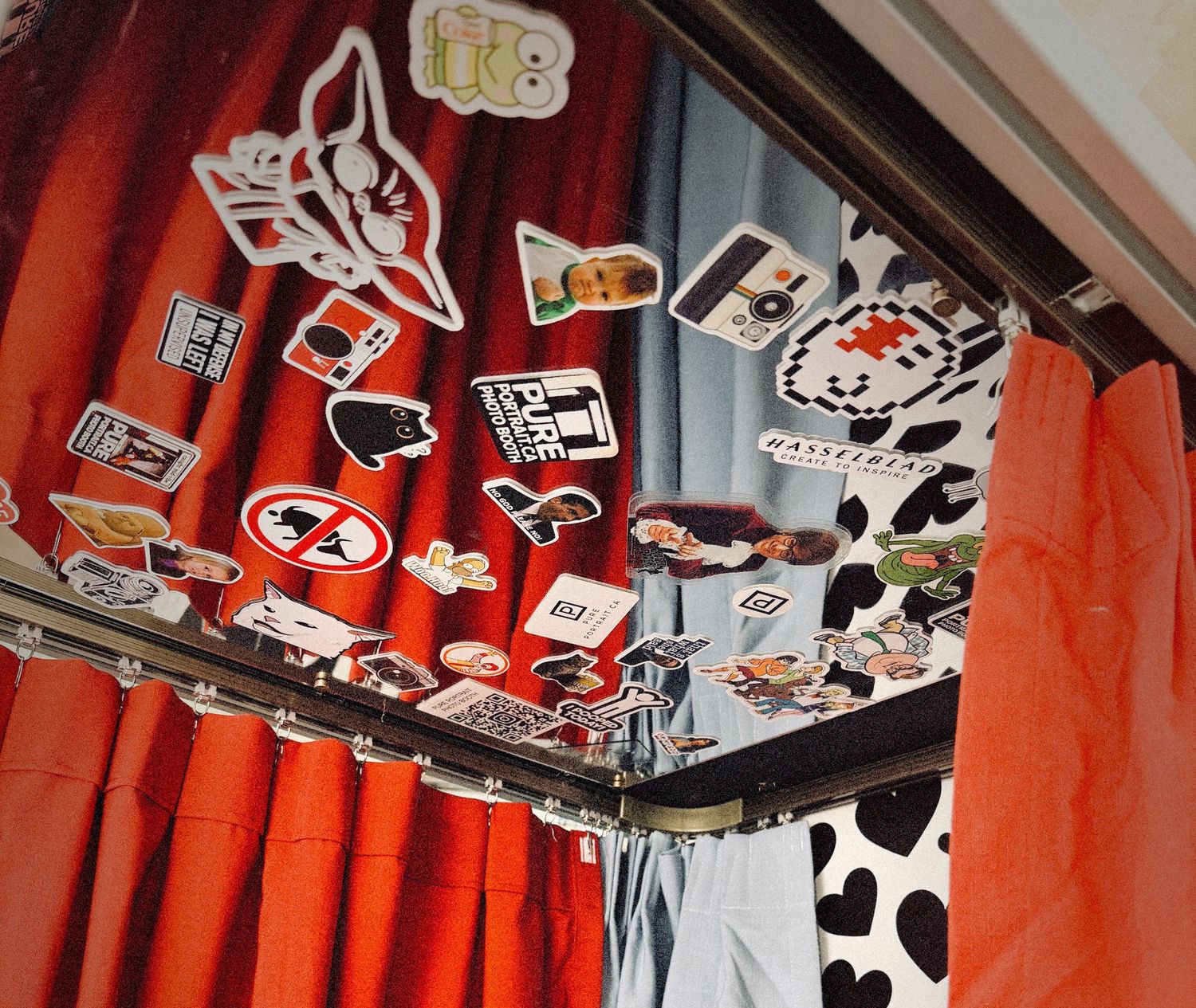 Colorful curtains with stickers on a curtain rod, featuring red, gray, and cow-print patterns in a decorated room.