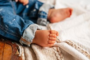 Close-up of a baby and toddler's bare feet resting on a soft knit blanket with denim jeans visible.