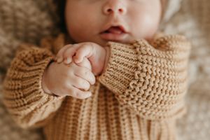 Close-up of a newborn baby's tiny hands in a cozy knit sweater.