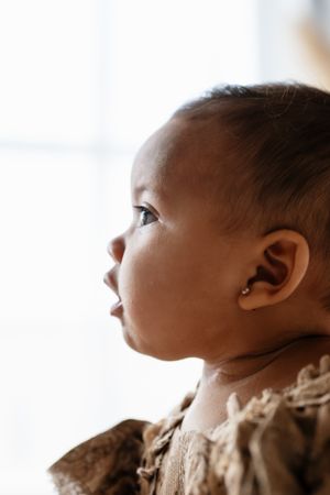 Close-up profile of an adorable baby with a small earring, gazing upward in soft natural light.
