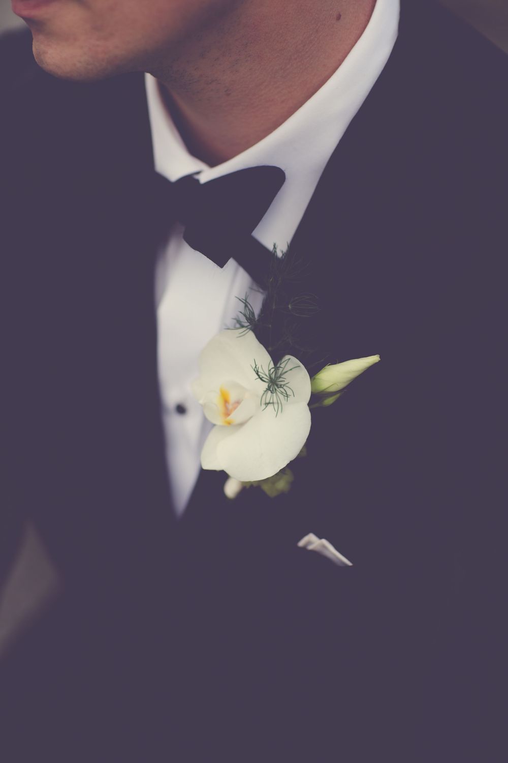 Groom in black tuxedo with bow tie wearing a white freesia boutonniere on his lapel.