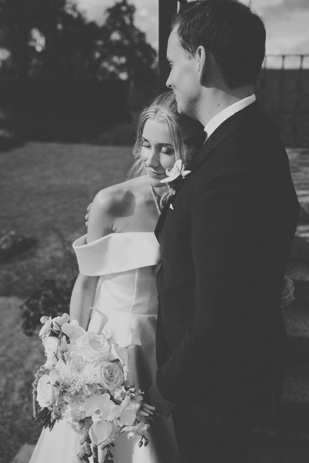 Black and white photo of a bride and groom sharing an intimate moment, bride holding a bouquet of roses.