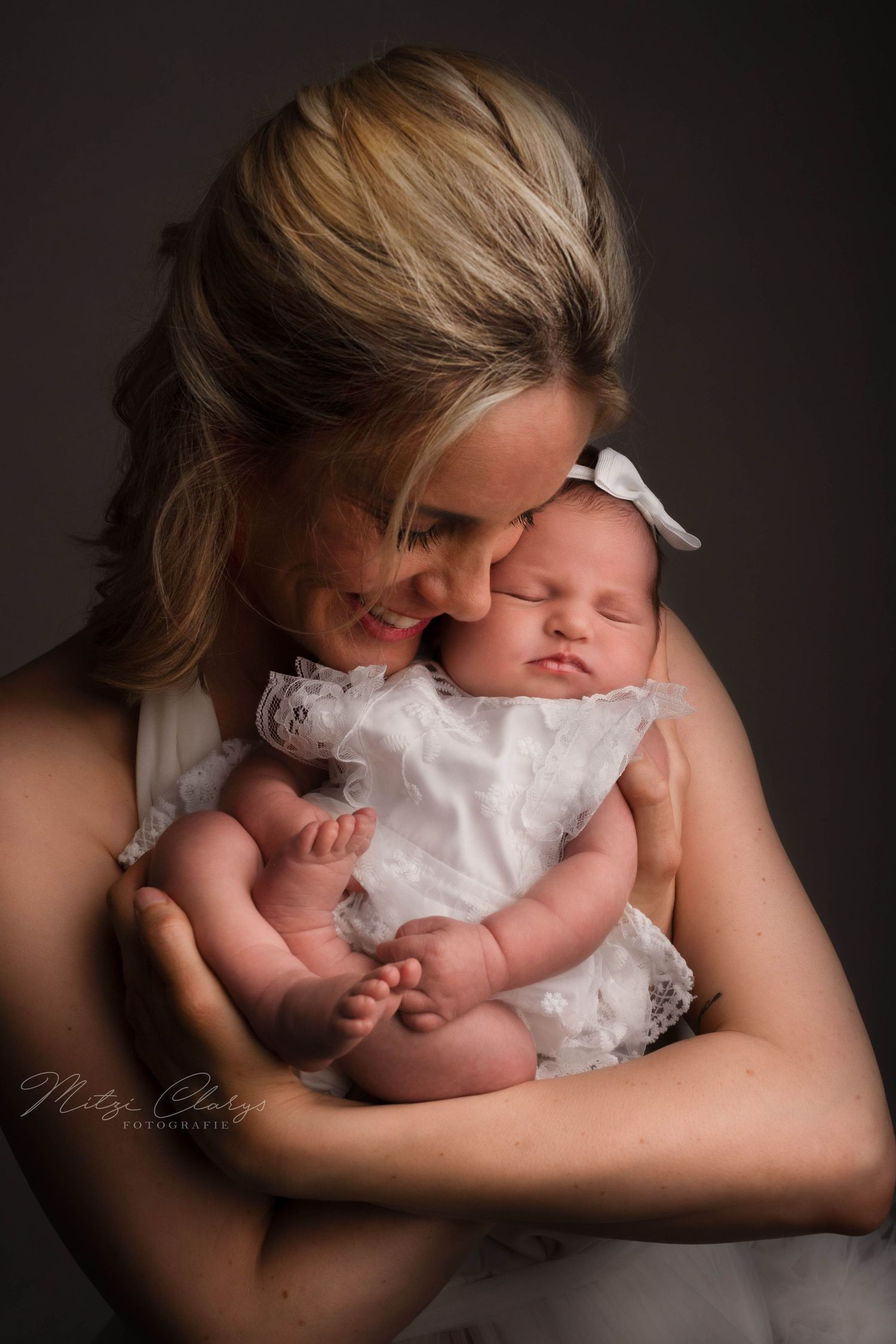 Moeder in witte jurk knuffelend met pasgeboren baby in een wit pakje tijdens een newbornshoot
