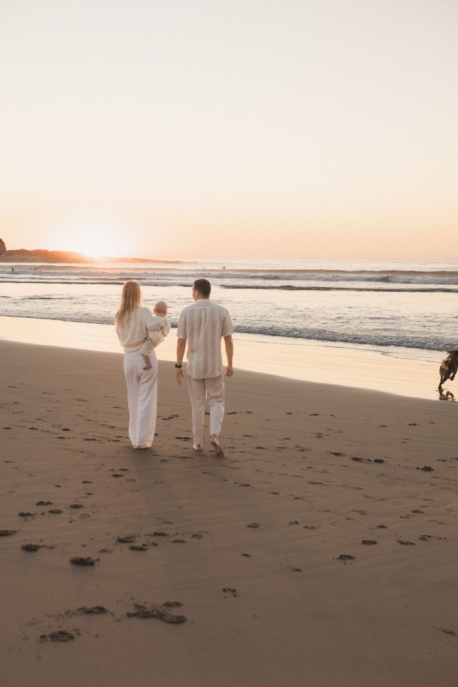 Black and white photo of a couple kissing while holding their baby on a beach.