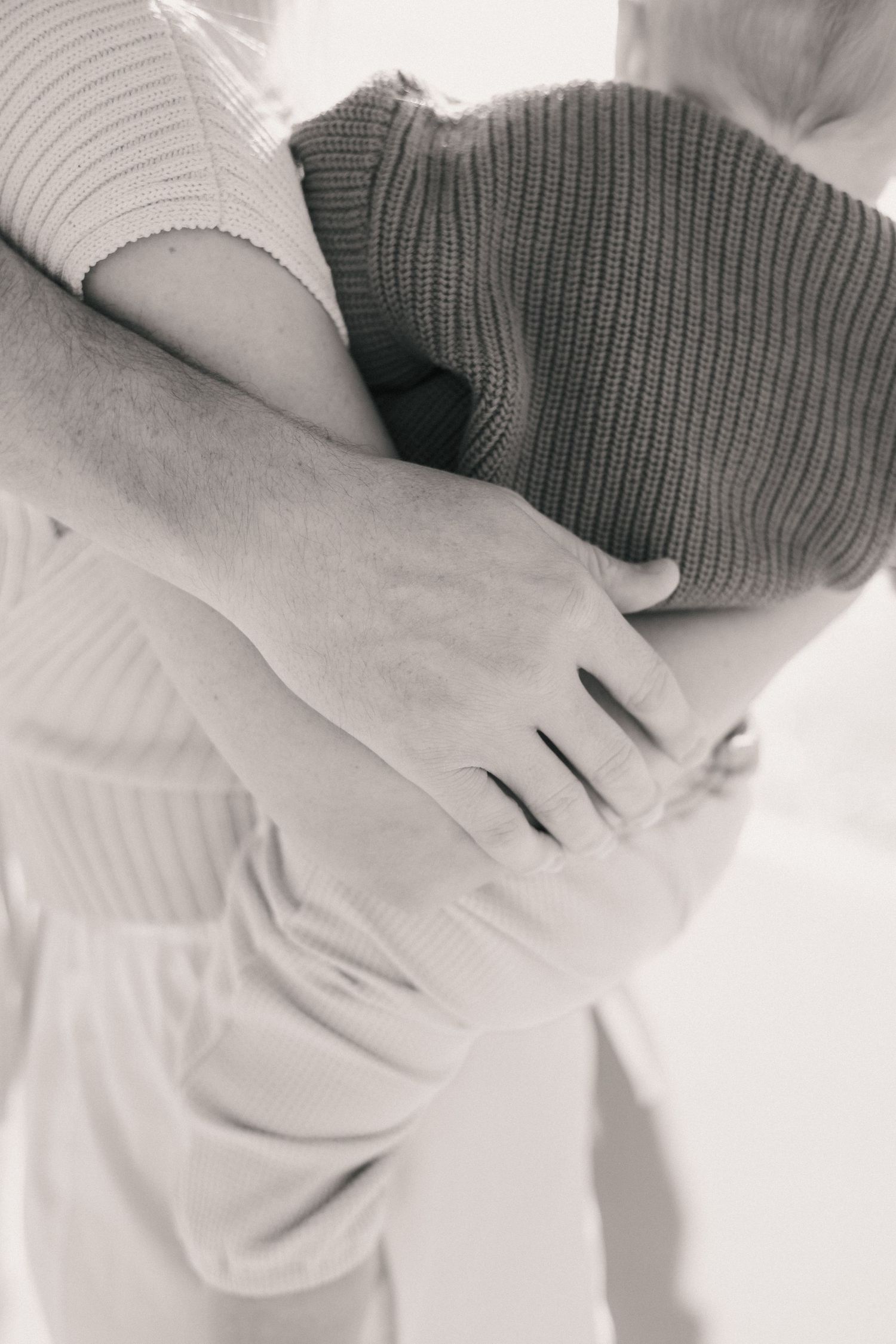 Black and white photo of a couple kissing while holding their baby on a beach.