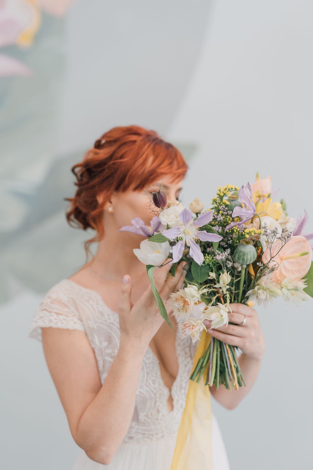 Red-haired bride in lace wedding dress smelling a colorful pastel bouquet with yellow ribbon.