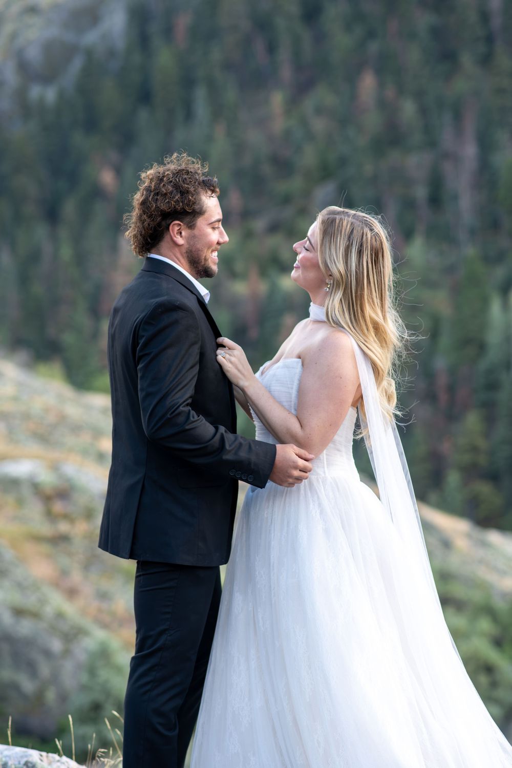Bride and groom gaze lovingly at each other in close portrait with forest backdrop.