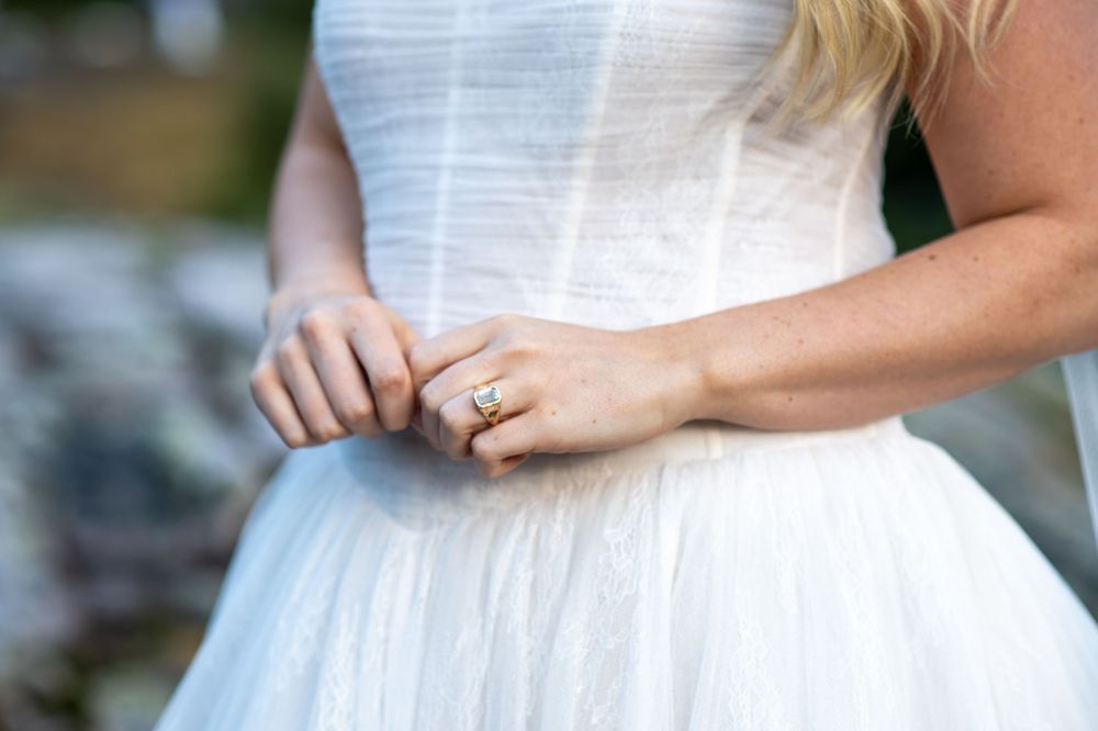 Bride in white tulle dress showcasing a gold diamond engagement ring on her finger.