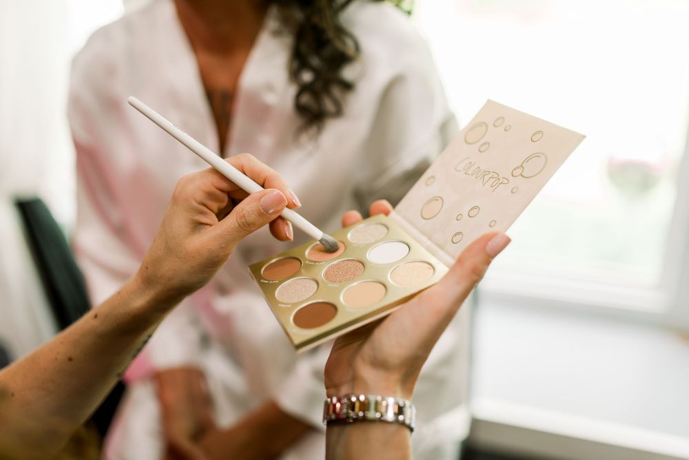 A makeup artist holds a neutral eyeshadow palette and brush during a bridal beauty preparation session.