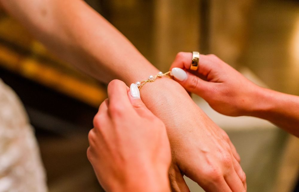 Hands clasping a gold chain bracelet with white stone charms onto a womans wrist.