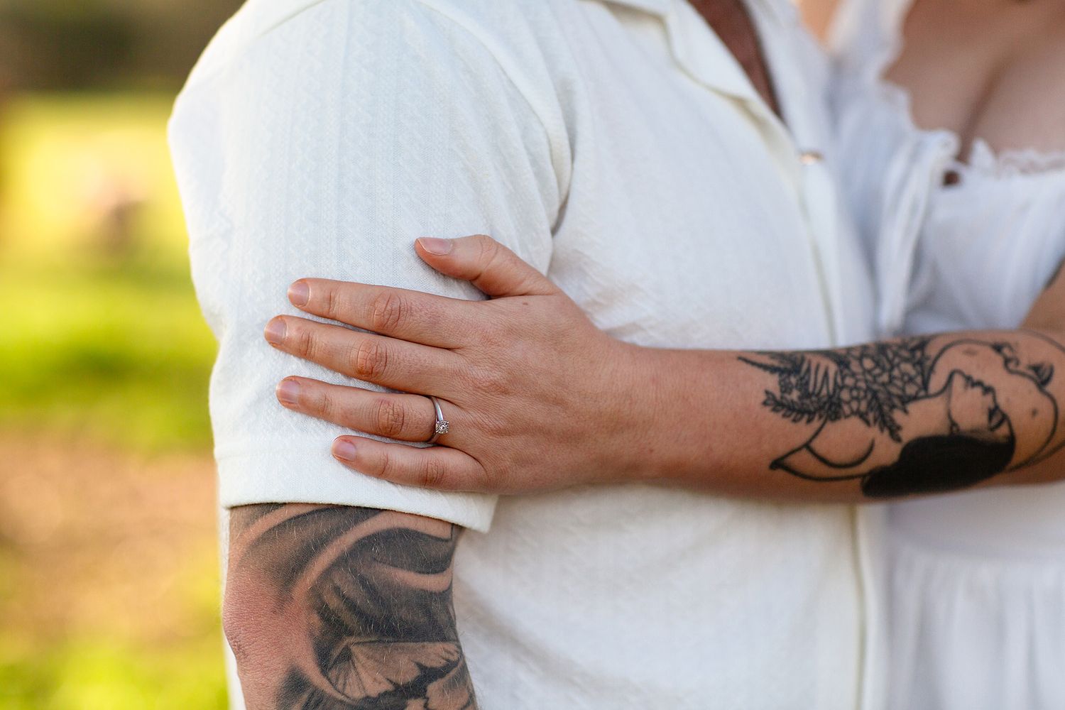 Couple holding hands with tattoos on their arm during engagement session showing engagement ring