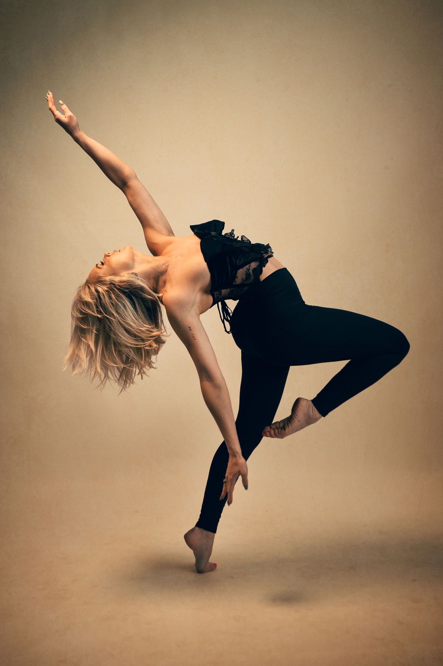 Blonde dancer in black outfit performs dynamic contemporary dance pose on studio background.