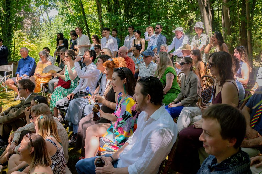 Guests seated outdoors at a garden wedding ceremony surrounded by trees.