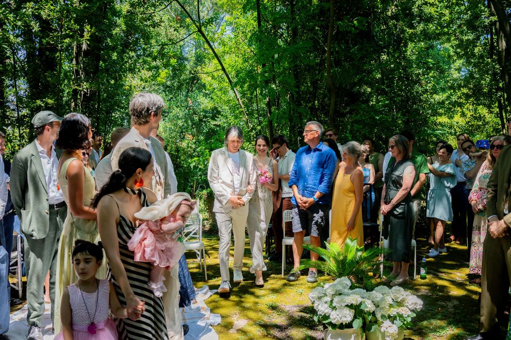 Outdoor wedding ceremony in a lush green forest with guests gathered around the couple.