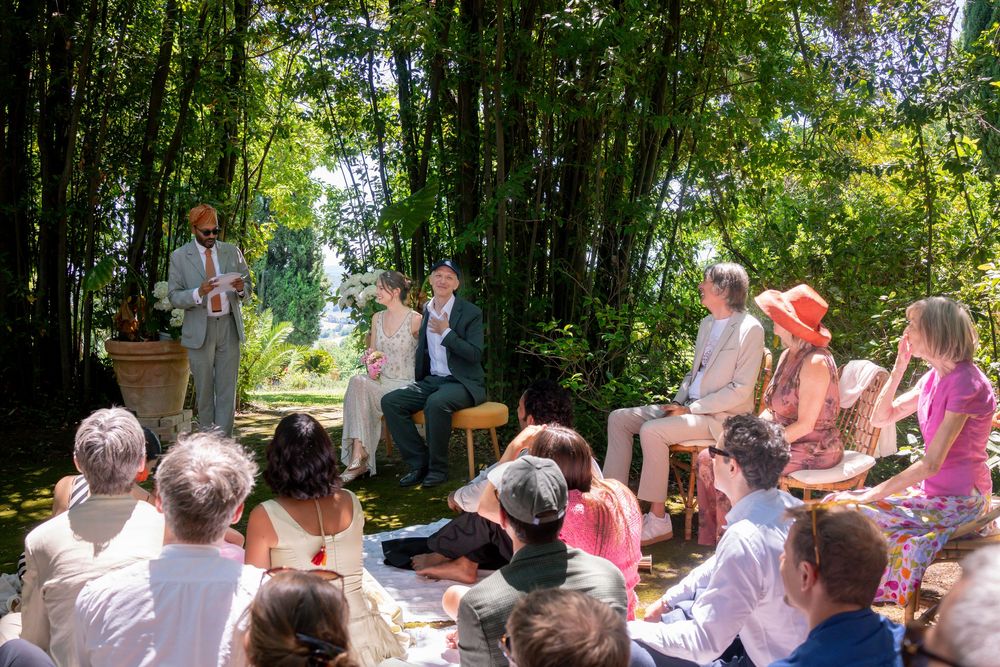 Outdoor gathering with people seated watching a small ceremony in a lush bamboo garden on a sunny day.