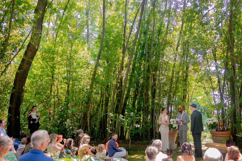 Outdoor wedding ceremony in a lush green forest with guests seated watching couple exchange vows.