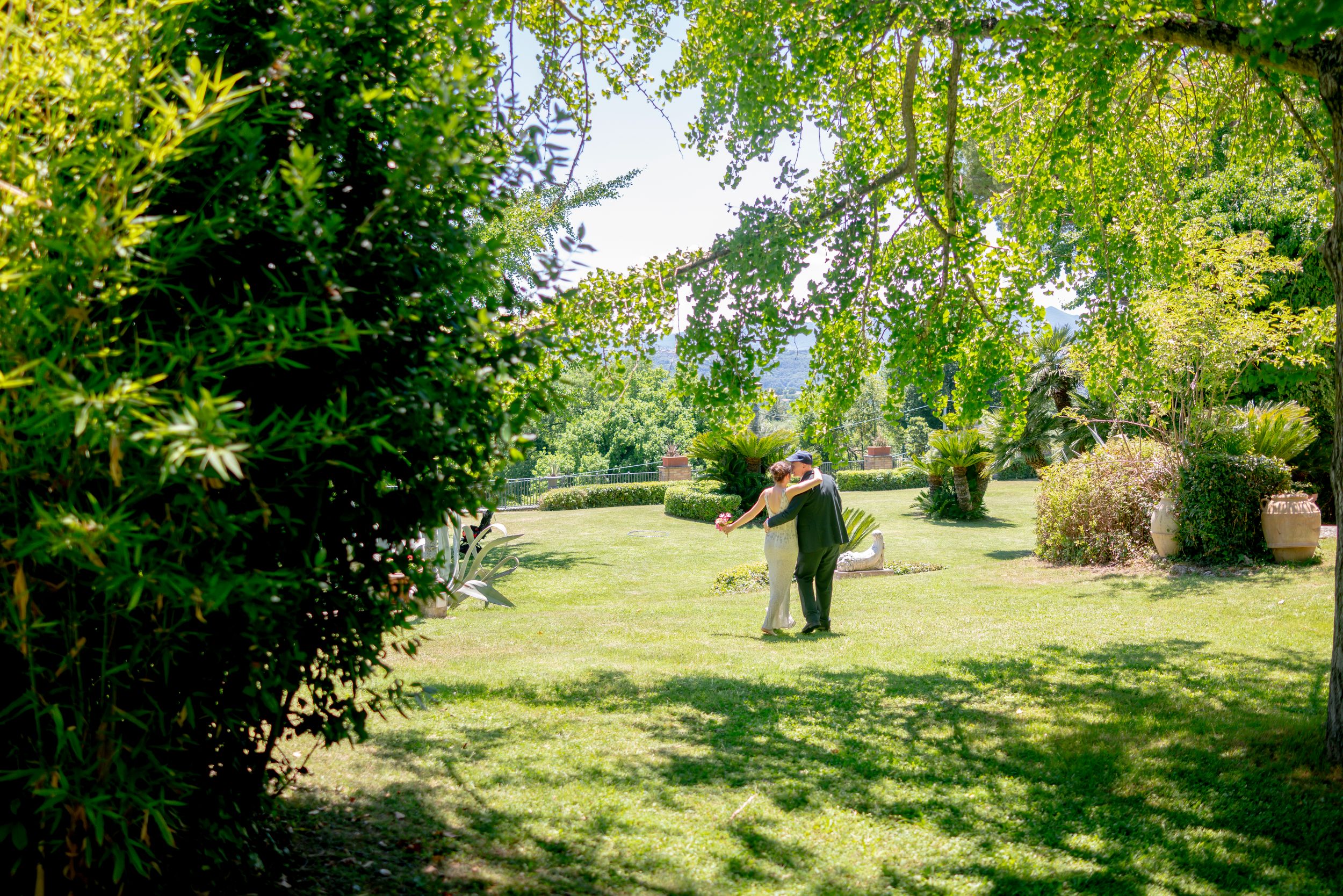 Two people dancing together in a beautiful sunlit garden surrounded by green trees.