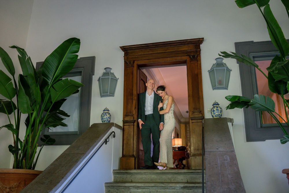 Couple stands in elegant doorway on stone steps surrounded by tropical plants and lanterns at a wedding venue.
