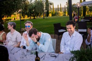 Guests laughing and enjoying dinner at an outdoor wedding reception in a scenic vineyard at sunset.
