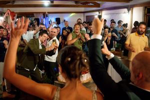 Bride and groom celebrate on the dance floor surrounded by cheering wedding guests at a lively indoor reception.