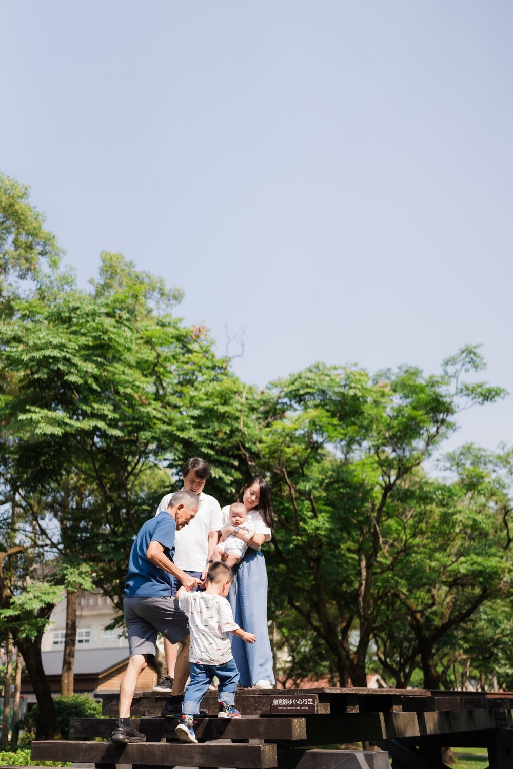 Asian family with children playing on wooden steps in sunny park.
