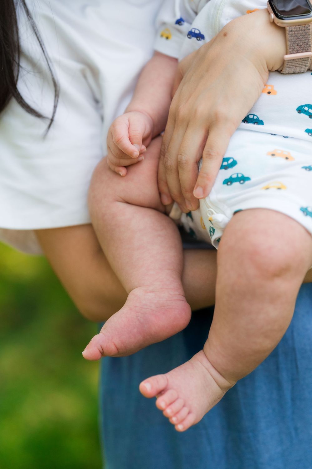 Close-up of mother holding baby's chubby legs and feet outdoors in a garden.