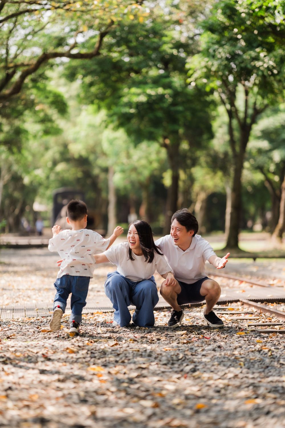 Happy Asian family with two young children share a joyful moment on a tree-lined park path.