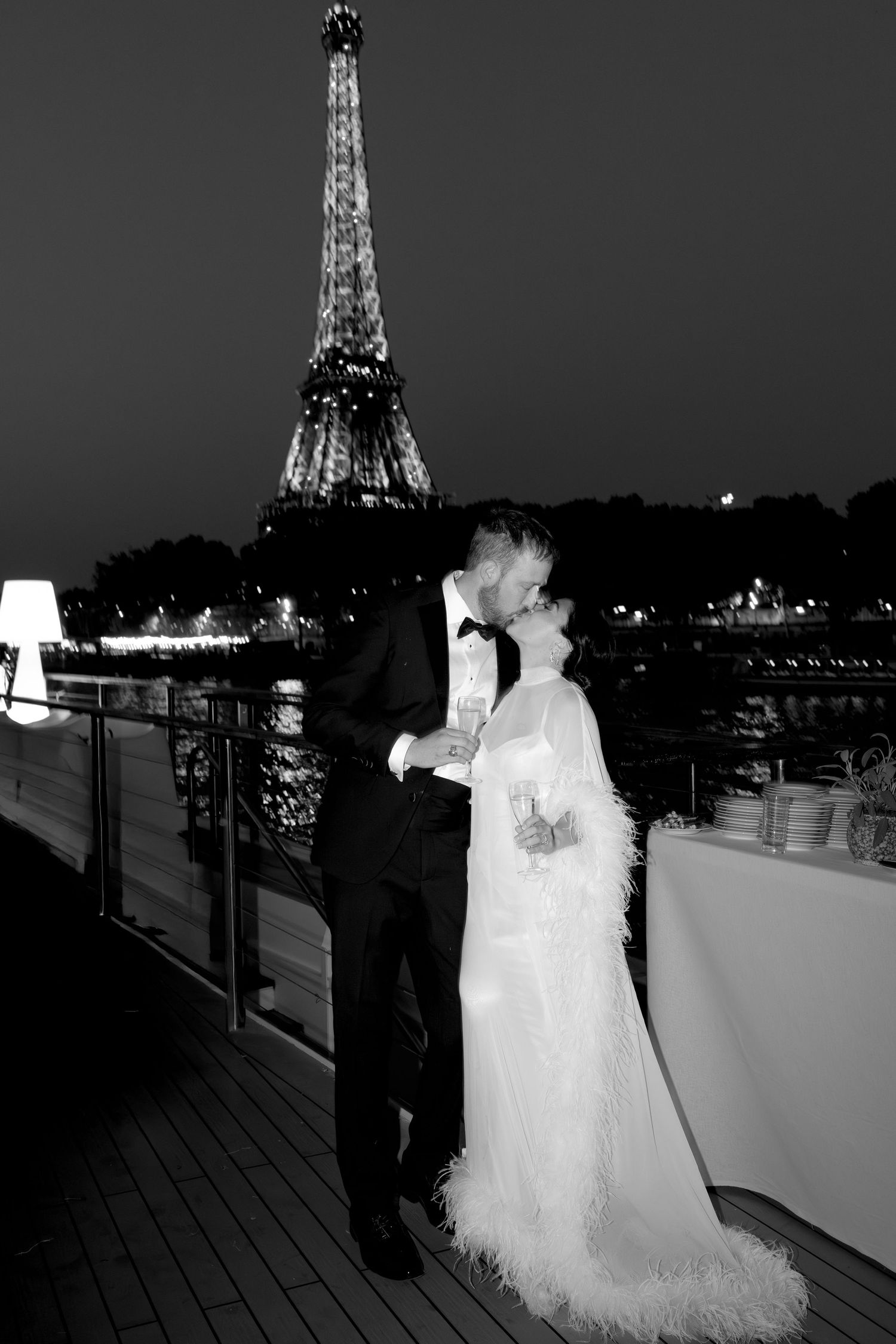 Black and white photo of a couple kissing in wedding attire with the Eiffel Tower illuminated at night in Paris. Paris nighttime wedding