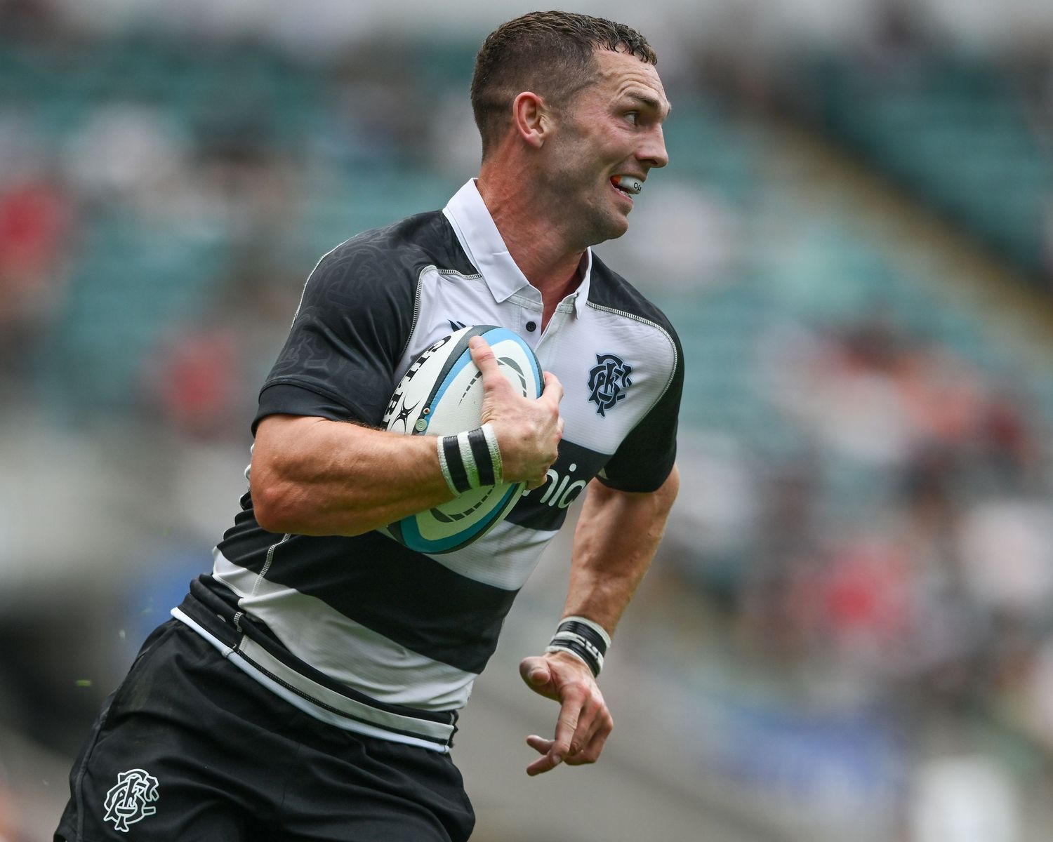 Rugby player in black and white kit running with ball during a match at a stadium.