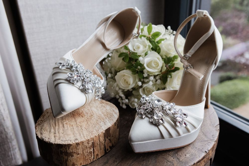 Brautschuhe mit Strassdetail und weißer Rosenstrauß auf Holzscheibe – Detail zur freien Trauung in Sonsbeck am Niederrhein.