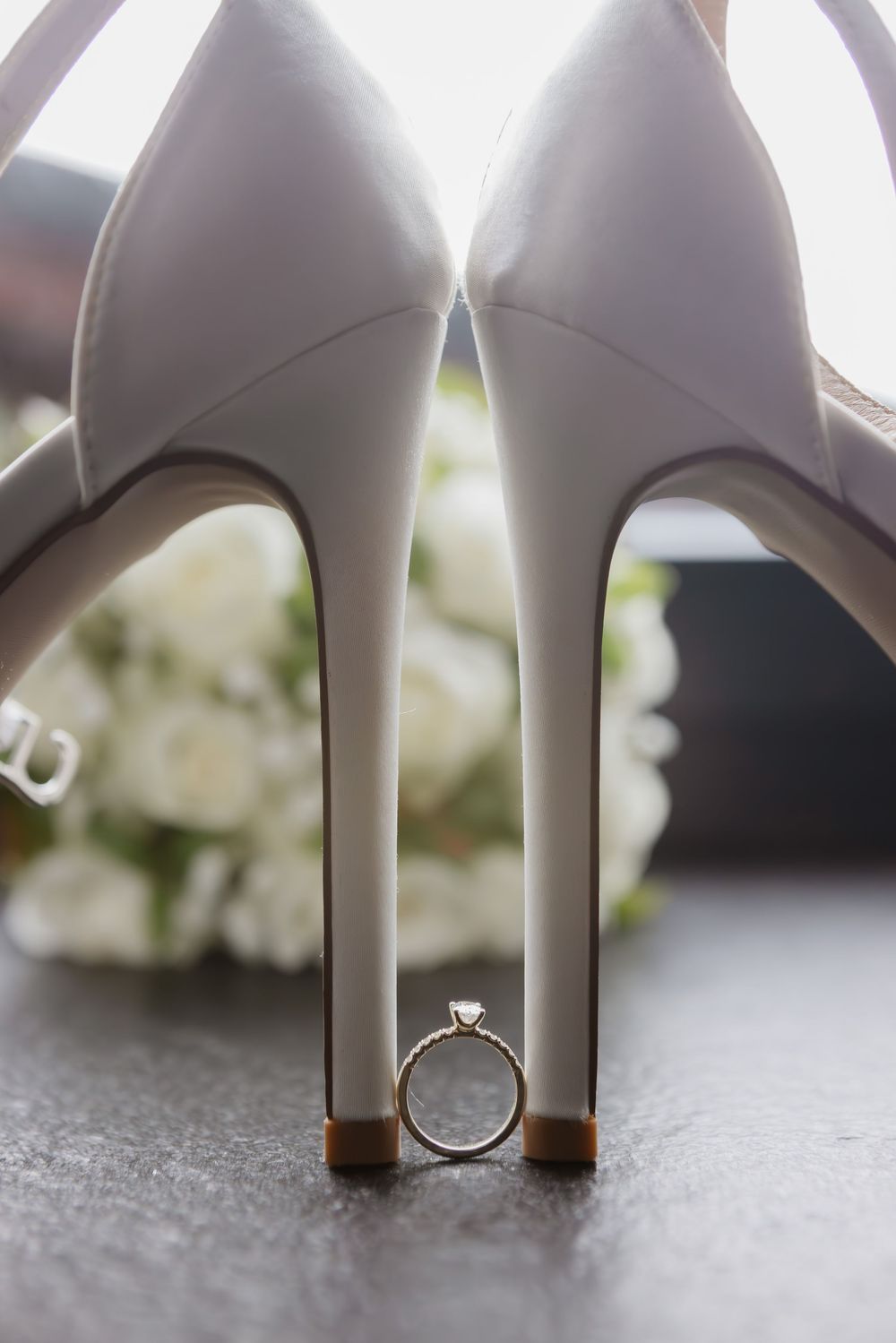 Verlobungsring steht zwischen zwei Brautschuhen, dahinter der Brautstrauß – Detailfoto zur Hochzeit im Waldrestaurant Höfer.