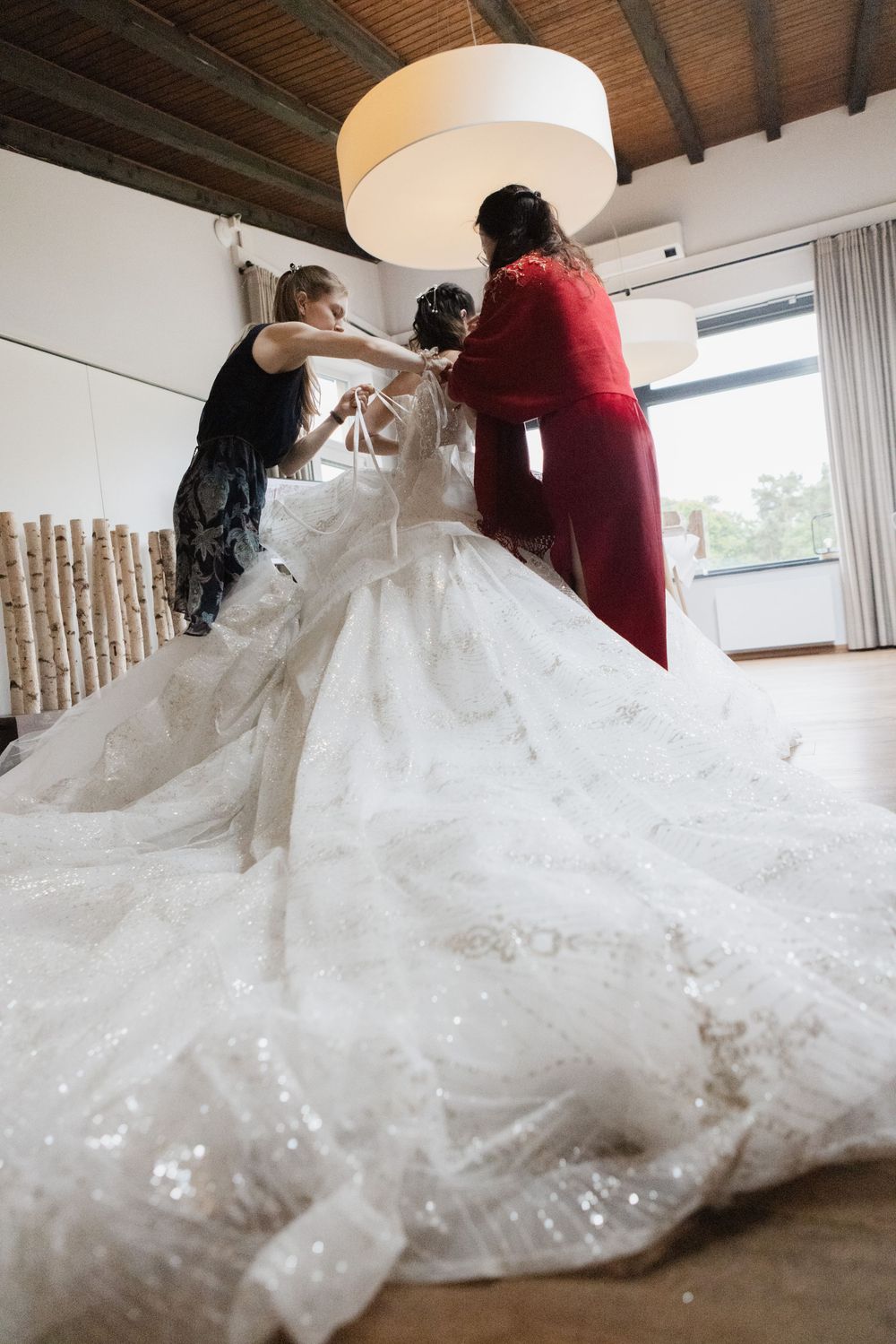 Braut wird in ihr funkelndes Ballkleid geholfen – Getting-ready zur deutsch-chinesischen Hochzeit im Waldrestaurant Höfer.