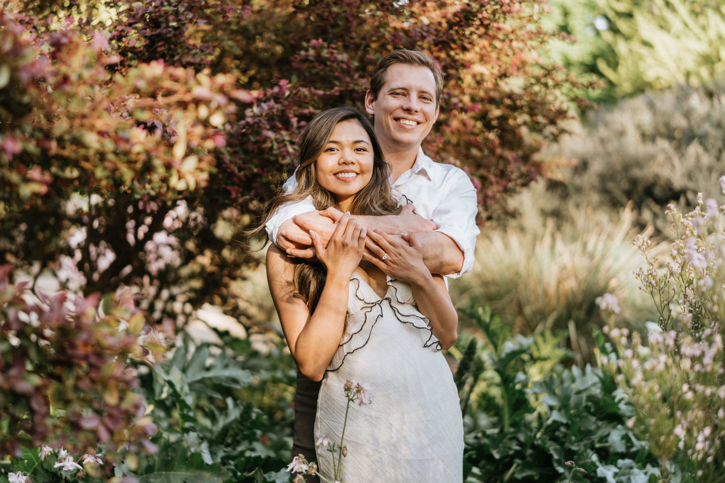 Mariel and Jeff smiling together among colorful botanical gardens.