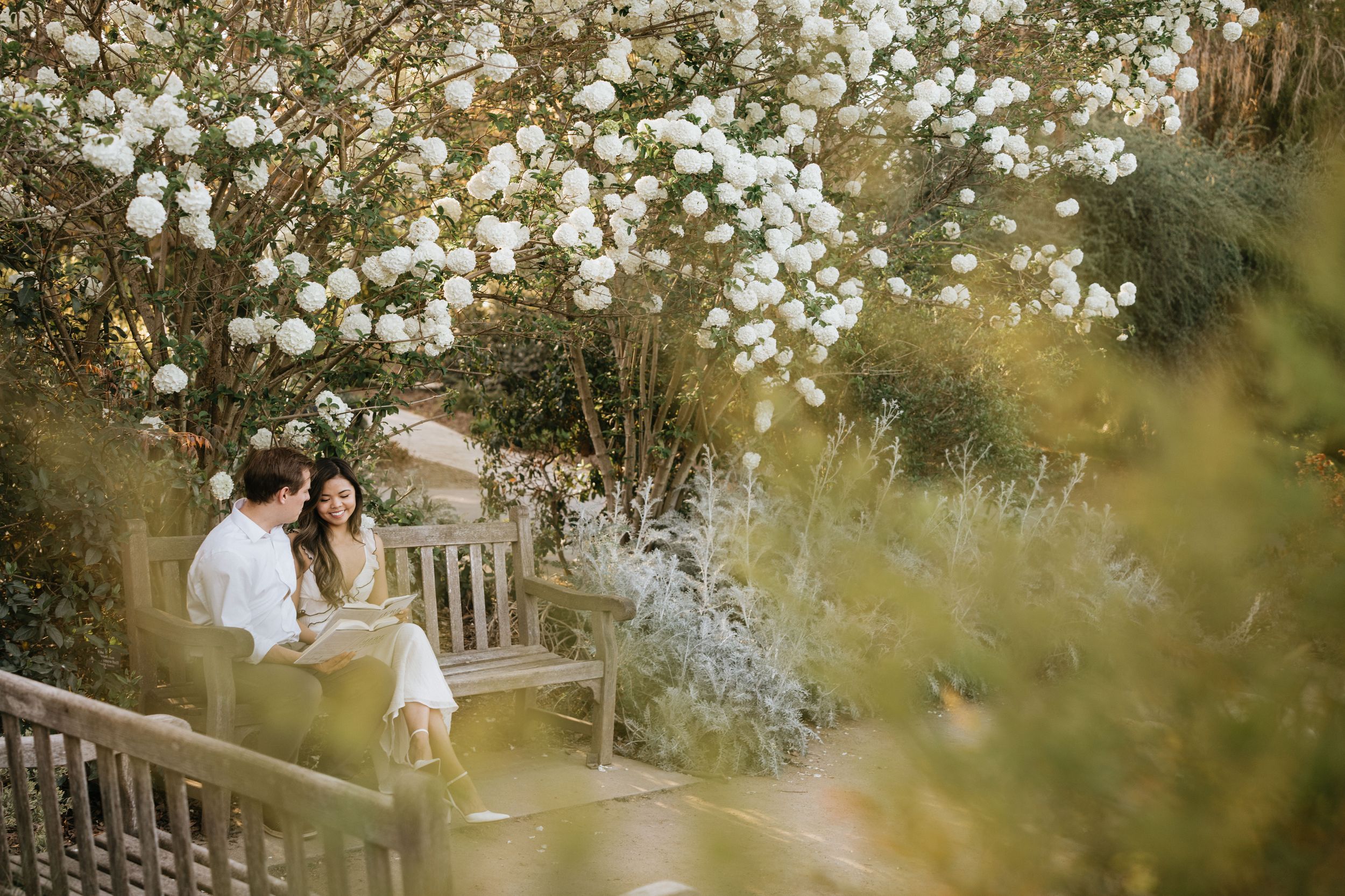 Mariel and Jeff relaxing on a garden bench beneath blooming white spring flowers.
