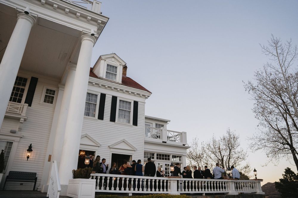 Elegant white colonial mansion with guests gathered on the porch at dusk during an outdoor event.