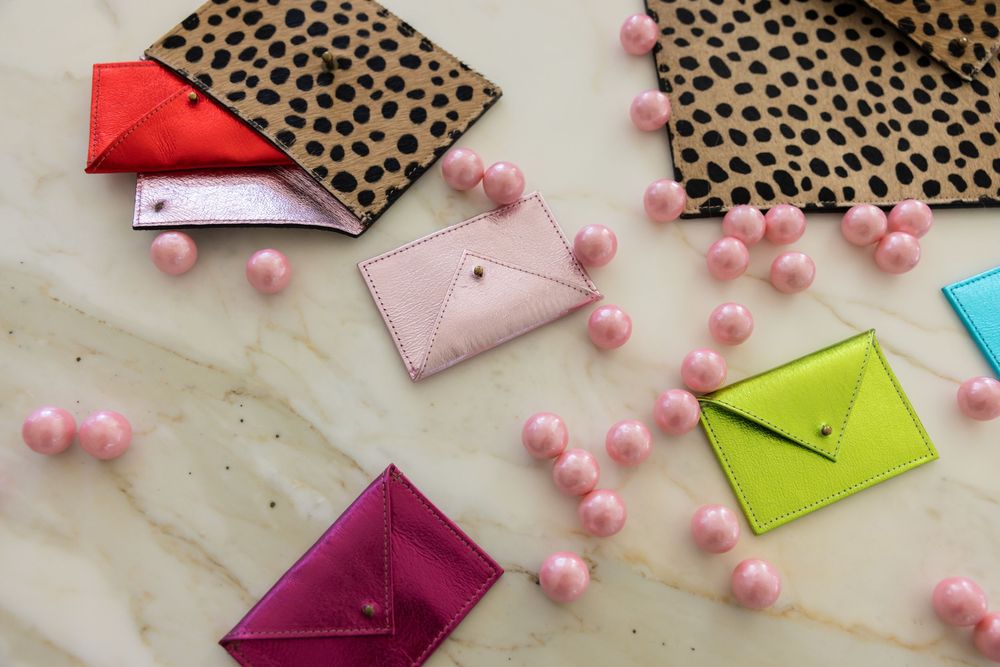 Assortment of colorful metallic envelope card holders scattered on marble surface with pink decorative beads.