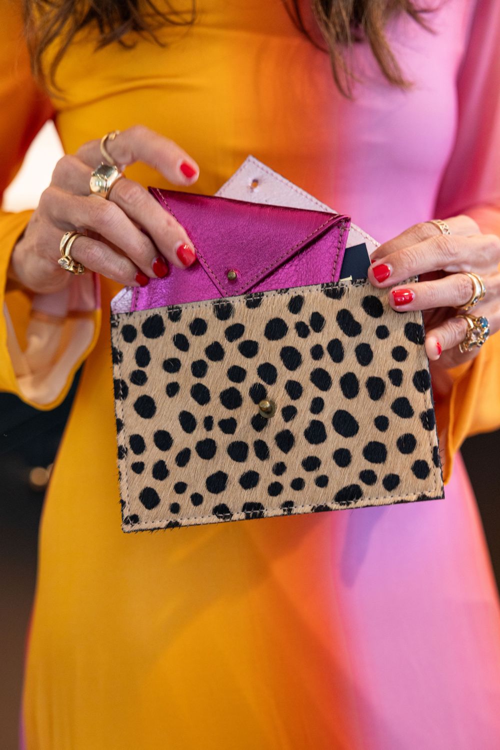 Woman with red nails holds open a cheetah print wallet revealing a pink interior.