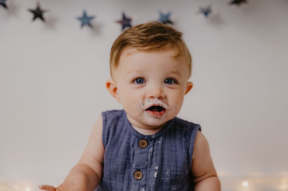 Cute baby boy with frosting on his face sitting in front of star decorations during a first birthday cake smash.
